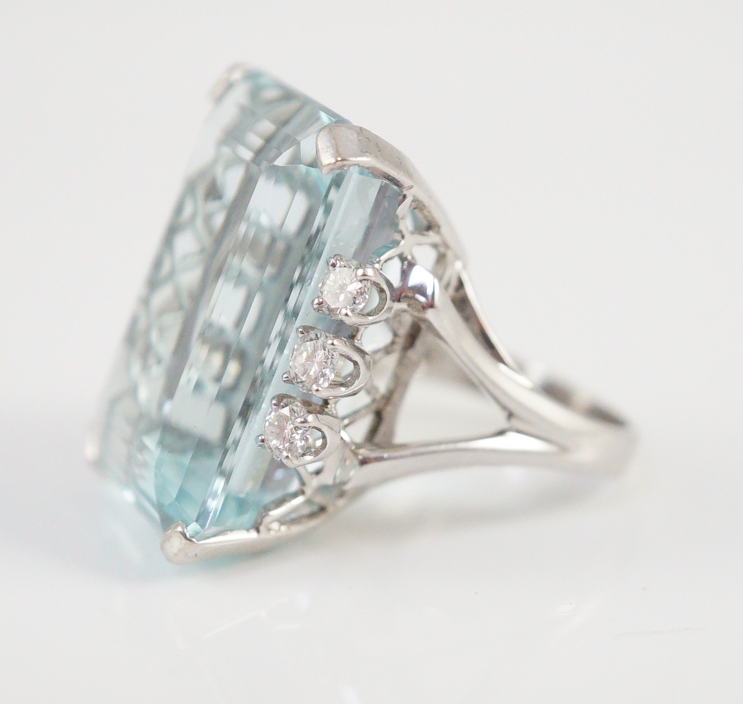 A large modern 14k white gold and emerald cut aquamarine set dress ring, flanked by six round cut diamonds